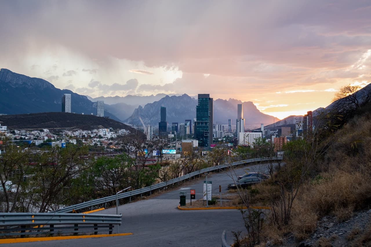 Vista de Monterrey al atardecer con rascacielos, montañas de fondo y una carretera en primer plano
