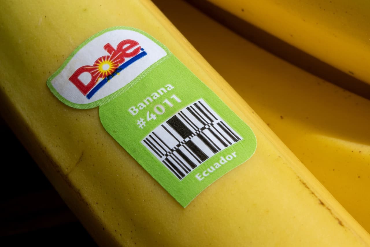 Se ve un plátano amarillo con una etiqueta de la marca 'Dole'. La etiqueta es de color verde y contiene información sobre el plátano, incluyendo el código #4011 y la mención 'Ecuador'.