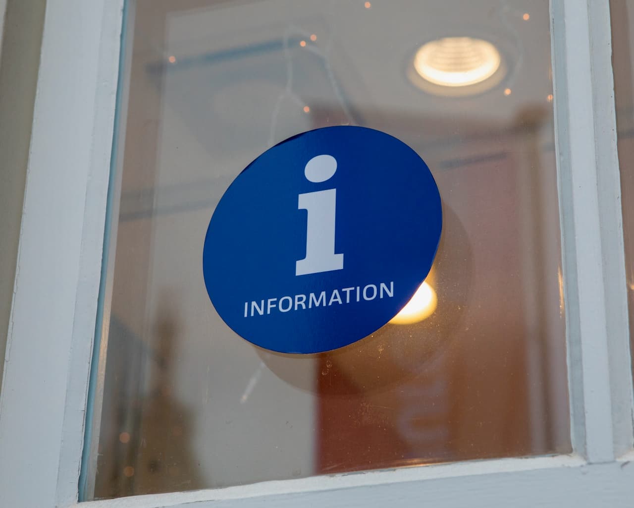 Un adhesivo circular azul en una ventana con la letra 'i' blanca y la palabra 'INFORMATION' debajo. Esta imagen resalta la marca 'punto clave', indicando un punto de información.