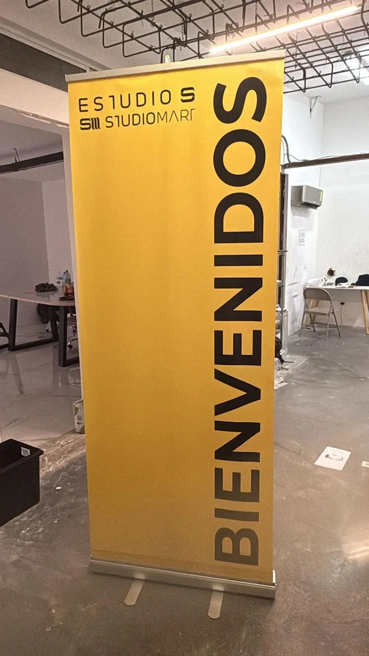 Banner roll-up amarillo con la palabra Bienvenidos instalado a la entrada de un estudio